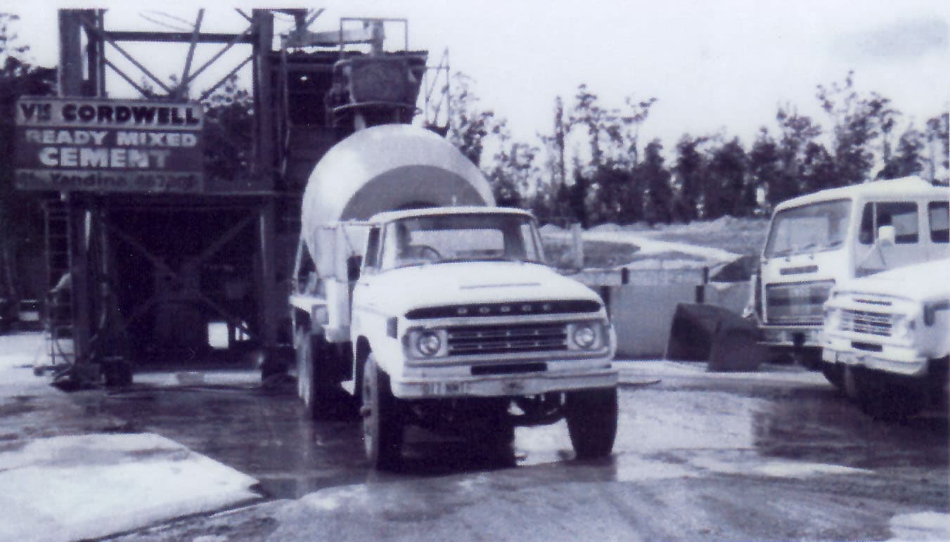 A old cement mixer truck parked in front of a cement plant, ready for loading or unloading materials.