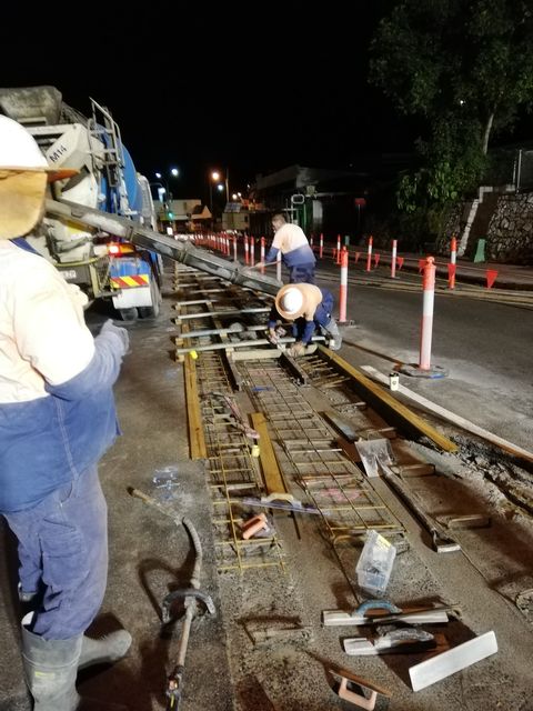 Two men engaged in road work at night, using tools under the glow of nearby streetlights.