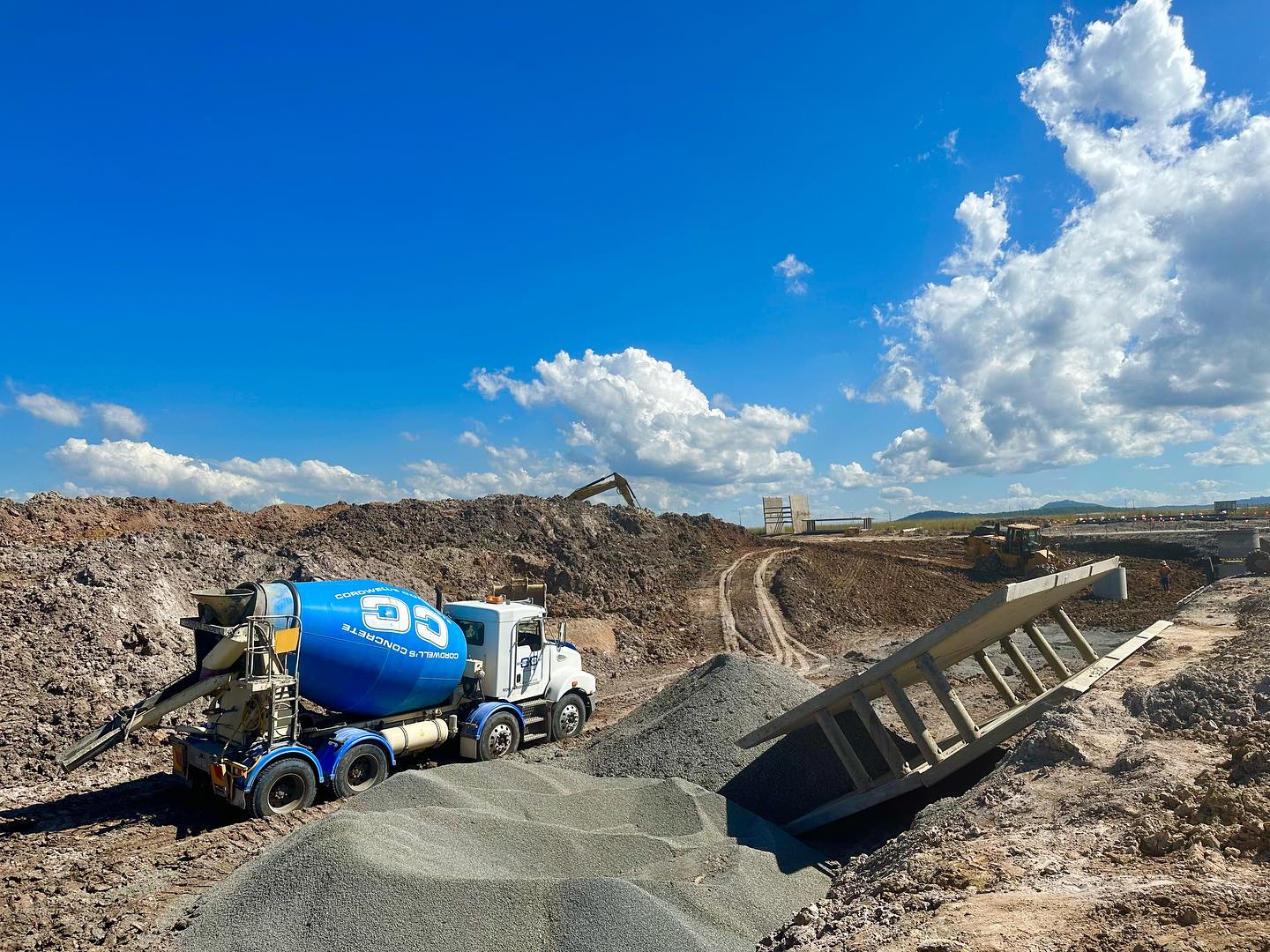 A cement mixer truck is stationary on a dirt road, located within a construction site environment.